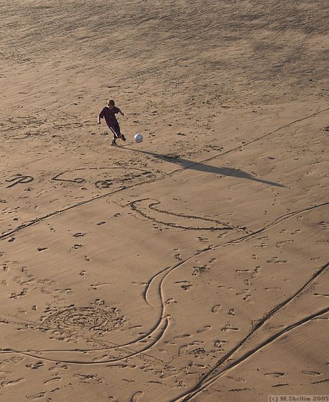 Kid playing football in the sand